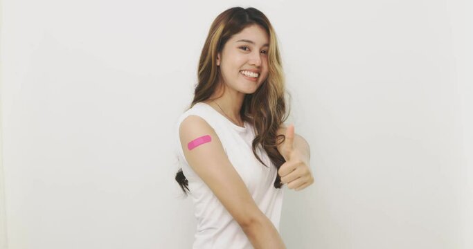 Asian Woman Shows Thumb Up And  Bandage On Arm. Happy Asian Woman Feels Good After Received Vaccine On White Background.