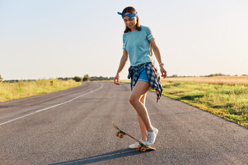 Full length photo of slim attractive woman doing tricks on a skateboard, having fun alone in the street, riding longboard, wearing casual clothing, looking down.