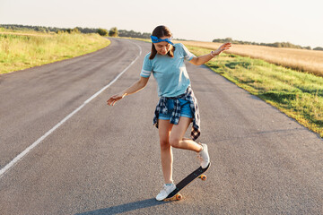 Obraz premium Outdoor shot of sporty woman in casual clothing having fun on asphalt road with skateboard, likes to spend time in active way, healthy lifestyle, happy pastime.