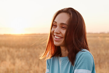 Fototapeta premium Summer portrait of laughing happy woman outdoor, enjoying warm sunshine, wearing blue t shirt, having dark hair, looking away with toothy smile, expressing happiness.