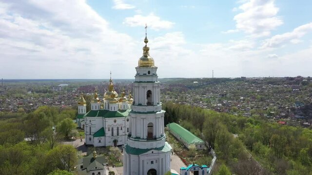 The territory of the church on a hill near the city. High white bell tower and golden domes with a cross
