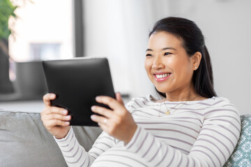 pregnancy, rest, people and expectation concept - happy smiling pregnant asian woman with tablet pc computer sitting on sofa at home