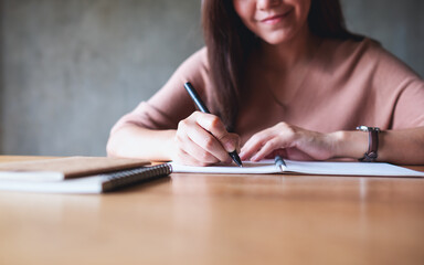 Closeup image of a beautiful woman writing on notebook on wooden table