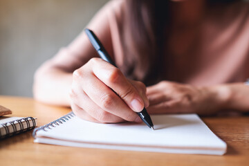 Closeup image of a woman writing on notebook on wooden table