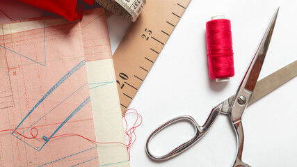 sewing hobby with tools, thread, scissors, red satin fabric white background top view