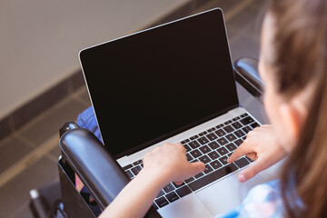 Disabled caucasian schoolgirl sitting in wheelchair using laptop, copy space on screen