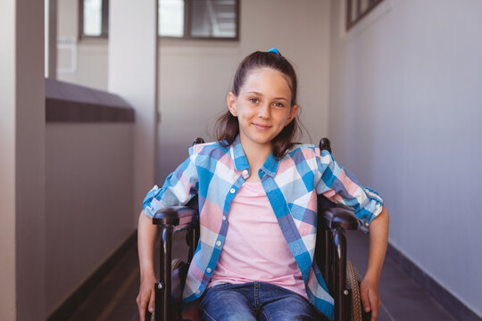 Portrait of smiling disabled caucasian schoolgirl sitting in wheelchair in school corridor - Powered by Adobe