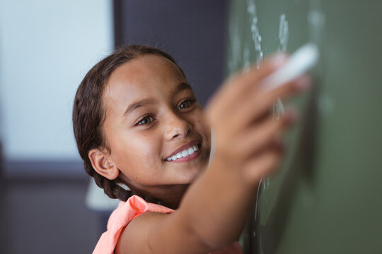 Portrait of mixed race schoolgirl standing writing on chalkboard in classroom