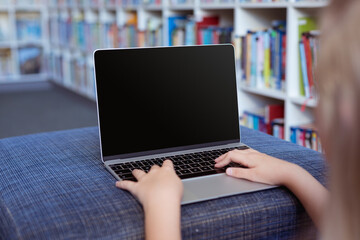 Caucasian schoolgirl at desk in school library using laptop, with copy space on screen