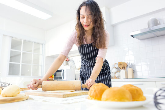 Smiling Young Woman Work With Wooden Roller Pin Making Sweet Pie Or Pastry Dough In Kitchen, Happy Millennial Female Loving Wife Cooking In Apron Preparing Family Dinner Or Dessert Baking Buns