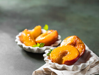 Caramelized peaches with honey, with mint leaves on a concrete background with shadows. Summer dessert.