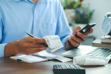 Man using smartphone and holding bills checking for cost in the home office,Start up counting finance.tax system.