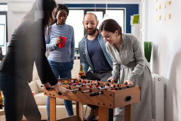 Multi ethnic group of people playing at foosball table after work partying and enjoying alcohol...