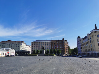 Red Square in the city of Vyborg, laid with paving stones, with a monument, surrounded by old houses.