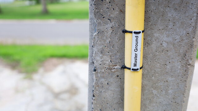 Ground conduit on pole-closeup. The master ground conduit of the short circuit protection system installed on the side of the concrete power pole with copy space. Selective focus