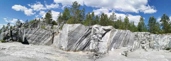 Fototapeta na wymiar Panorama of an Italian quarry with smooth sections and vertical cuts of marble in the Ruskeala Mountain Park on a sunny summer day.