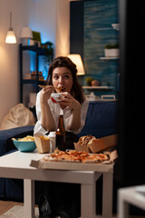 Smiling woman sitting on couch eating tasty chinese food during fast-food home delivered in living room. Caucasian female watching at television enjoying chopstick. Takeaway food delivery