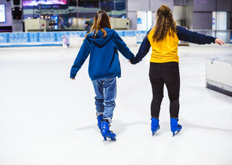 Girl friends ice skating on the ice rink together - obrazy, fototapety, plakaty