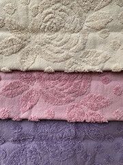 Three different colored, folded hygenyc towel with rose pattern. Cotton fiber spa towel fabric texture. Handmade bath towel with flower pattern for self care. Pastel pink, purple and beige cloth.