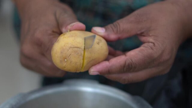 Closeup shot of hands of an Indian man chopping potato in half using kitchen knife