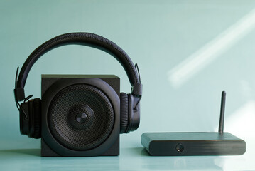 Wireless headphones and a square black audio speaker next to a Wi-Fi router or mini-computer in the sunshine. Concept for digital music and wireless audio transmission. Daylight