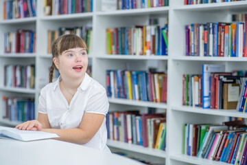Happy young girl with syndrome down sits with a book at library.  Education for disabled children concept. Empty space for text