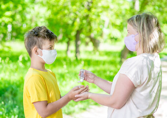 Naklejka premium Woman wearing protective face mask applies sanitizer for cleaning sons hands in public place