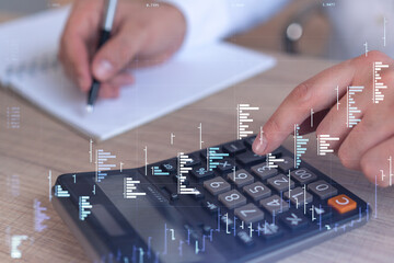 A trader computing historic data to predict stock market behavior. Internet trading concept. Forex and financial hologram chart over the desk and calculator.