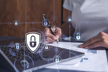 A businesswoman in casual wear signing the contract to prevent probability of risks in cyber security. Padlock Hologram icons over the working desk.