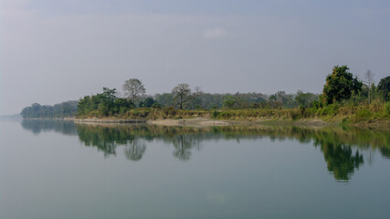 Peaceful landscape panorama of Brahmaputra river bank with trees reflection in water in remote rural Assam, India