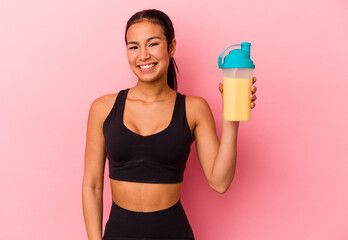 Young Venezuelan woman drinking a protein shake isolated on pink background happy, smiling and...