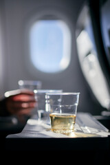 Disposable cups of drinks (water and wine) on table against airplane window. Refreshment during flight.