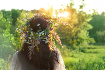 Woman in flower wreath outdoor, rear view. Floral crown, symbol of summer solstice. traditional...