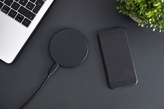 Recharging smartphone battery using round induction wireless charger. Top down view of office workplace.