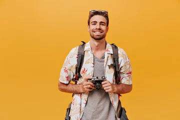 Foto op Plexiglas Smiling tourist with ginger beard in short sleeve summer shirt and plaid t-shirt holding camera and smiling on orange backdrop.. © Look!