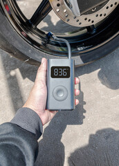 Hand holding a portable inflator is inflating a motorcycle tire.