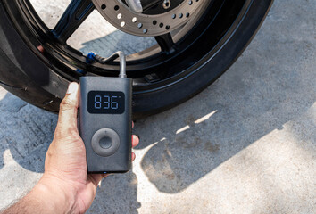 Hand holding a portable inflator is inflating a motorcycle tire.