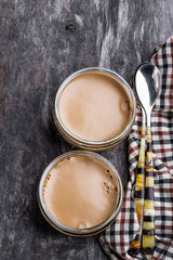 A pair of caramel cheesecakes in a glass pot on black wooden background