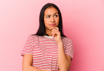 Young Venezuelan woman isolated on pink background thinking and looking up, being reflective, contemplating, having a fantasy.