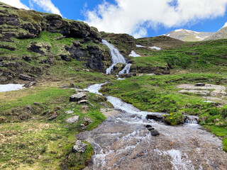 Fototapeta na wymiar Small waterfall in Swiss alps. Mountain landscape. Hiking on a sunny day near the river. Green mountains, and rocks on a background of bright blue sky.
