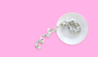 White measuring tape in a round plate on a pink background with copy space