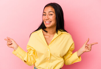 Young Venezuelan woman isolated on pink background pointing to different copy spaces, choosing one of them, showing with finger.