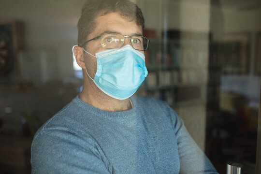 Portrait of caucasian man wearing glasses and face mask looking through window