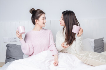 Obraz na płótnie Canvas Two beauties sitting in bed drinking milk tea