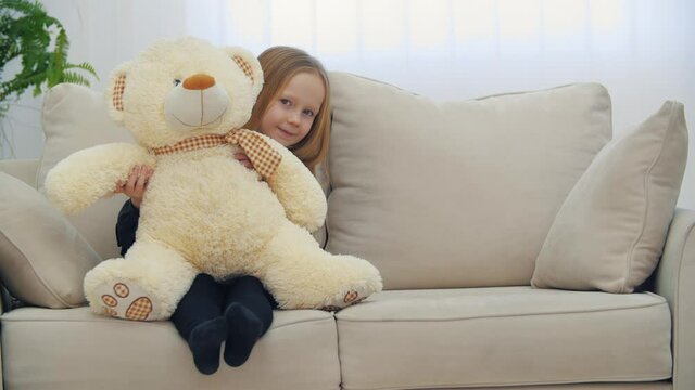 Small smiling girl sitting on the sofa with her toy teddy bear in 4k slowmotion video.