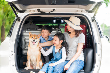 Happy family with Shiba inu dog in car outdoors. A family with a mother, daughter and son playing in the back of the car with Shiba Inu.