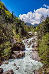 The rough river flows from mighty rocks of Ghagra ridge in Abkhazia. Rapid muddy stream, mountains covered with lush vegetation. Travel, hiking, tourism, passion, love, scenic destinations.