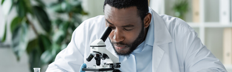 African american scientist looking through microscope in lab, banner
