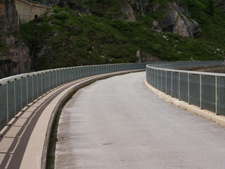 Fototapeta na wymiar single lane road with railings at the roadside, in a curve. Road on the embankment dam at Lac de Moiry, Switzerland