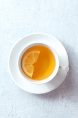 Tea with lemon, overhead shot of a plain white cup on a table. Natural remedy. Soothing citrus drink